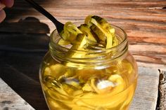 a jar filled with pickles sitting on top of a wooden table next to a spoon