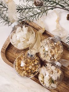 three glass ornaments sitting on top of a wooden tray next to pine cones and branches