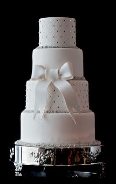 a three tiered white wedding cake on a silver platter with bows and sequins