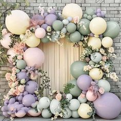 a wreath made out of balloons with flowers and greenery on the outside wall, in front of a brick wall