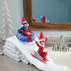 two elfs are sitting on top of towels in the bathroom, while one is holding his leg up