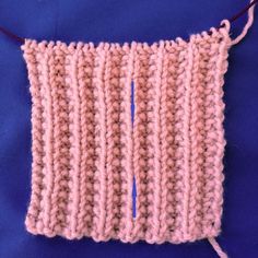 a close up of a knitted piece of cloth on a blue surface with a needle