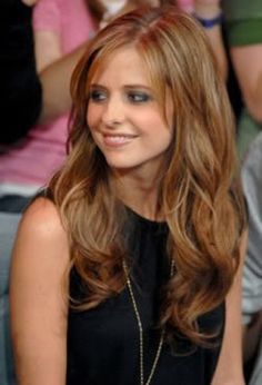 a woman with long brown hair sitting in front of a group of people and smiling at the camera