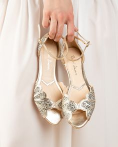 a close up of a person's hand holding a pair of gold wedding shoes