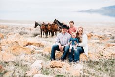 a family sitting on rocks with horses in the background