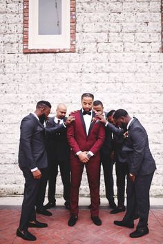 a group of men standing next to each other wearing suits and bow ties in front of a white brick wall