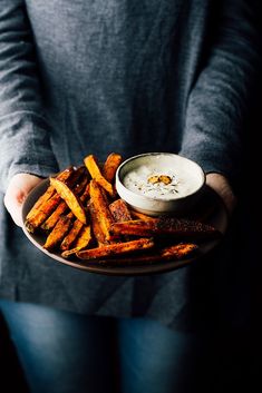 a person holding a plate with fries and dip