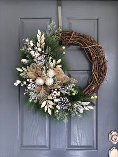 a wreath on the front door with pine cones and greenery hanging from it's side