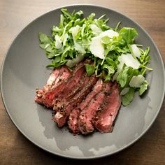 a plate with meat, lettuce and other vegetables on it sitting on a wooden table