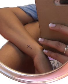 a woman's hand with a small cross tattoo on her left wrist, in front of a mirror