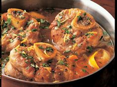 a pan filled with meat covered in sauce and garnished with lemons, parsley