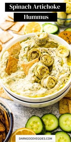 spinach artichoke hummus in a bowl with crackers and cucumbers