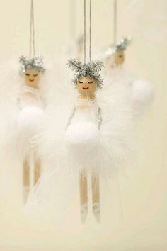 three angel ornaments hanging from strings with white feathers and silver decorations on top of them