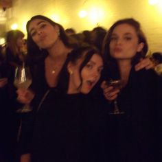 three women standing next to each other holding wine glasses and posing for the camera at a party