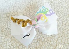 a white bow with gold glitter letters and a unicorn horn on it's side