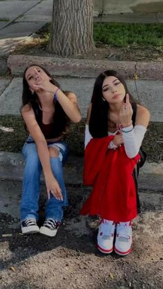 two young women sitting on the curb with their hands up to their ears and one pointing at her ear