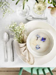 a white plate topped with a bowl filled with water next to two silver spoons