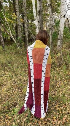 a woman is standing in the woods with her back to the camera, wearing a colorful blanket