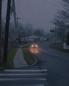 the car is driving down the street in the rain at night, with its headlights on