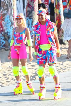 two people wearing roller skates and colorful clothing walking on the beach with palm trees in the background