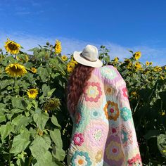 a woman standing in front of a field of sunflowers wearing a colorful blanket