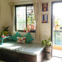 a room with a bed, window and potted plants on the windowsills