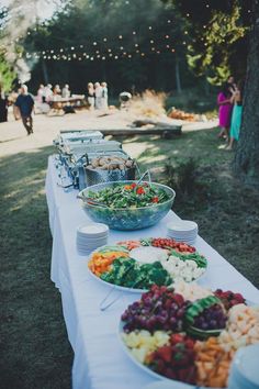 a long table filled with lots of food on top of a grass covered field next to trees