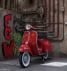 a red scooter parked next to a wall with graffiti on it