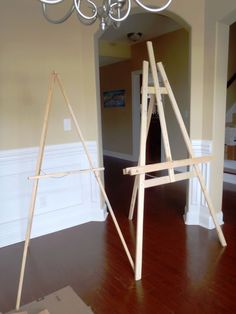 two wooden easels sitting on top of a hard wood floor next to a chandelier