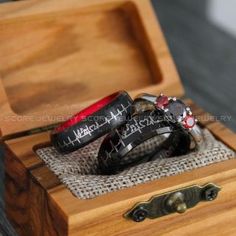 two black and red wedding bands in a wooden box with the words happily married written on them