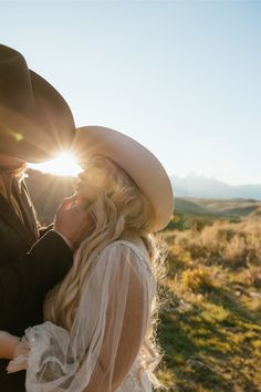 a bride and groom are standing in the sun on their wedding day, wearing cowboy hats