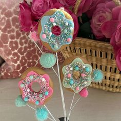 three donuts decorated with sprinkles and pom - poms on sticks