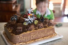 a young boy sitting in front of a birthday cake with dirt bikes on the top