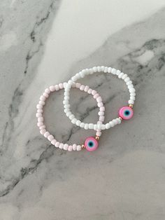 This pink evil eye bracelet is designed to bring anyone who wears it positive energy & protection. Available with either white or light pink 4mm glass beads Materials Used: White/Light Pink Beads: Glass Gold Beads: 14K gold plated Eye: Polymer Clay Stretch bracelet: Made to order in your wrist size Customization available: If you would like to adjust something in the design feel free to message me and I will do my best to accommodate!