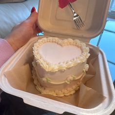 a heart shaped cake in a takeout container with a fork on the table next to it