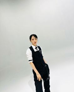 a woman standing in front of a white background wearing overalls and a black tie