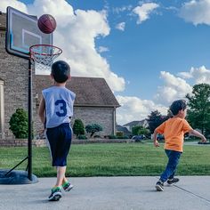 two young boys playing basketball in front of a house