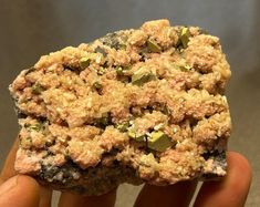 a person holding up a rock with rocks and gravel on it's sides, in front of a gray background