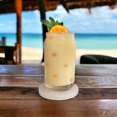 a drink with an orange garnish on the rim sits on a wooden table