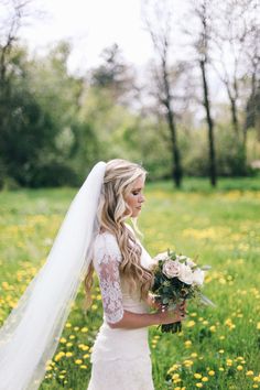 a woman in a wedding dress is standing in a field with flowers and holding a bouquet