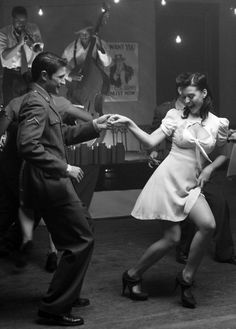 a man and woman dancing in an old - fashioned dance studio with other people around them