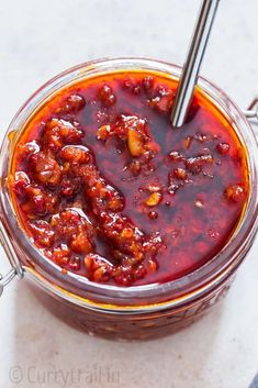 a glass jar filled with chili sauce on top of a white counter next to a spoon