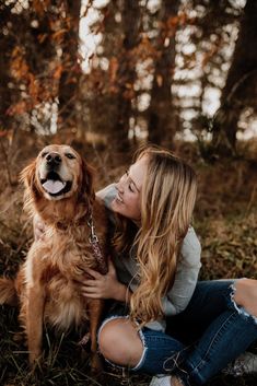 a woman sitting on the ground with her dog in front of her and smiling for the camera