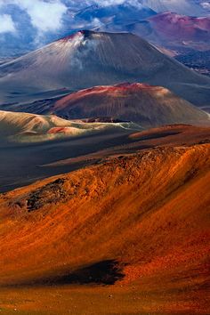 the mountains are covered in orange and brown colors, with clouds above them on a cloudy day