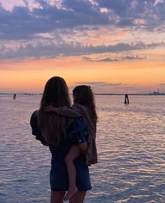 a mother and child standing on the beach at sunset