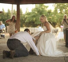 a man kneeling down next to a woman in a wedding dress on the ground near other people