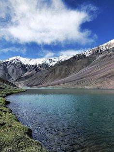 the mountains are covered in snow and green grass next to a lake with clear water