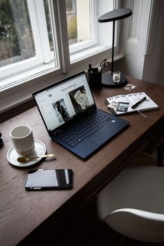 an open laptop computer sitting on top of a wooden desk next to a cup and saucer