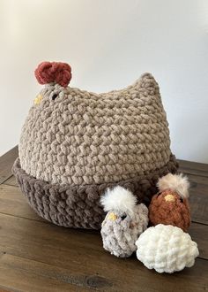 a crocheted chicken hat sitting on top of a wooden table next to stuffed animals