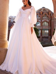 a woman in a white wedding dress standing on a stone wall with an arch and building in the background